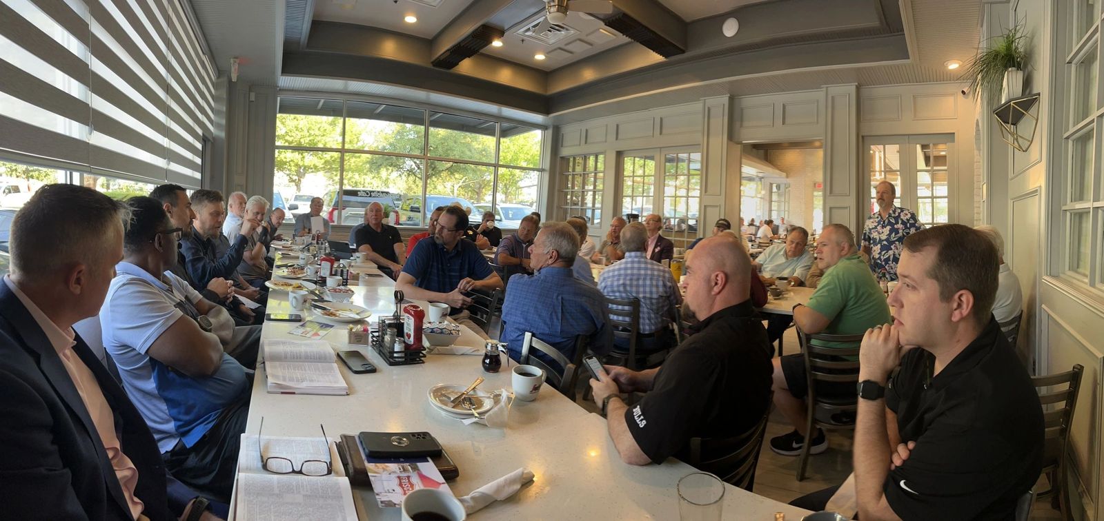Large group meeting in a bright restaurant with people engaged in discussion.